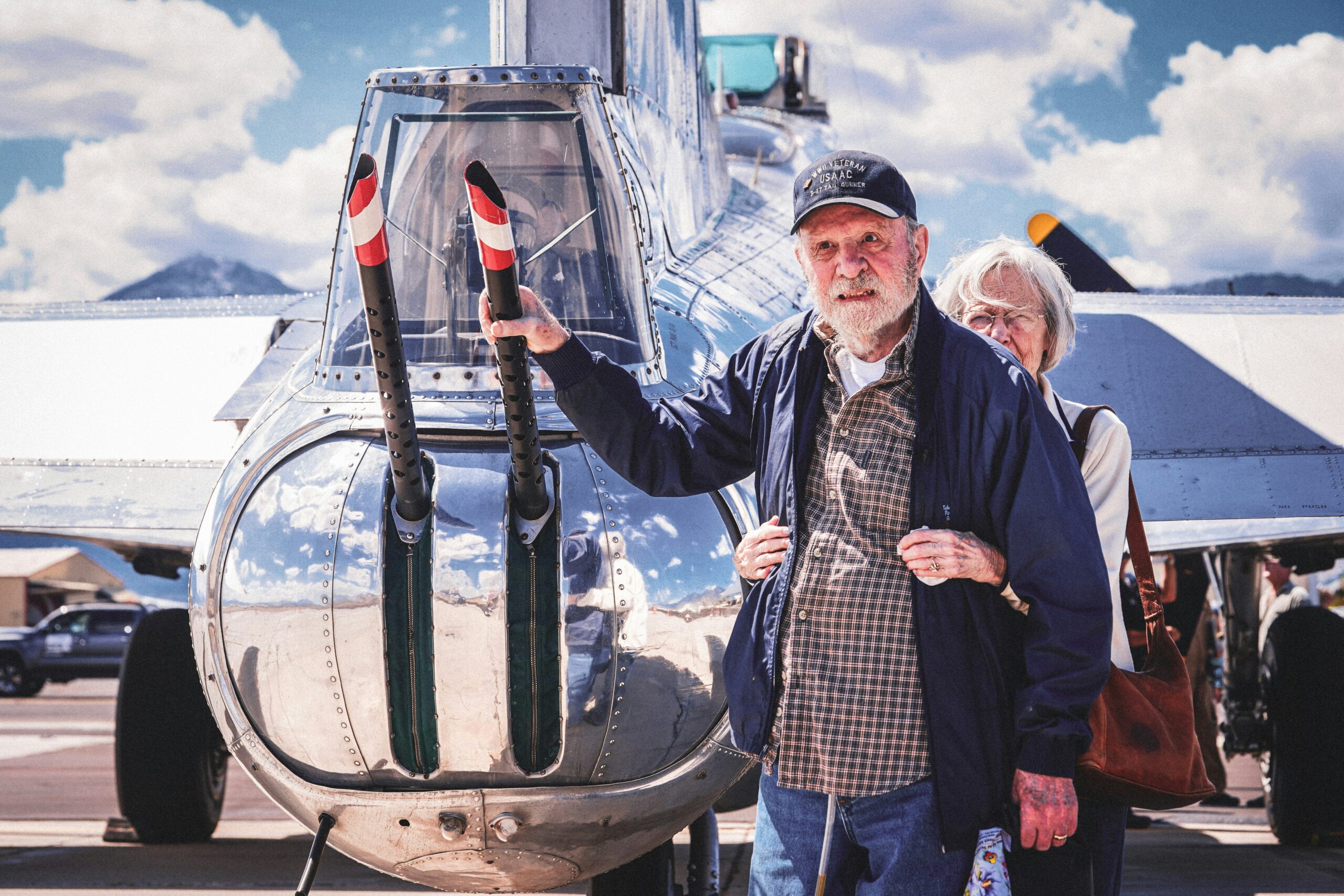 An elderly veteran man and woman stand next to a military plane.