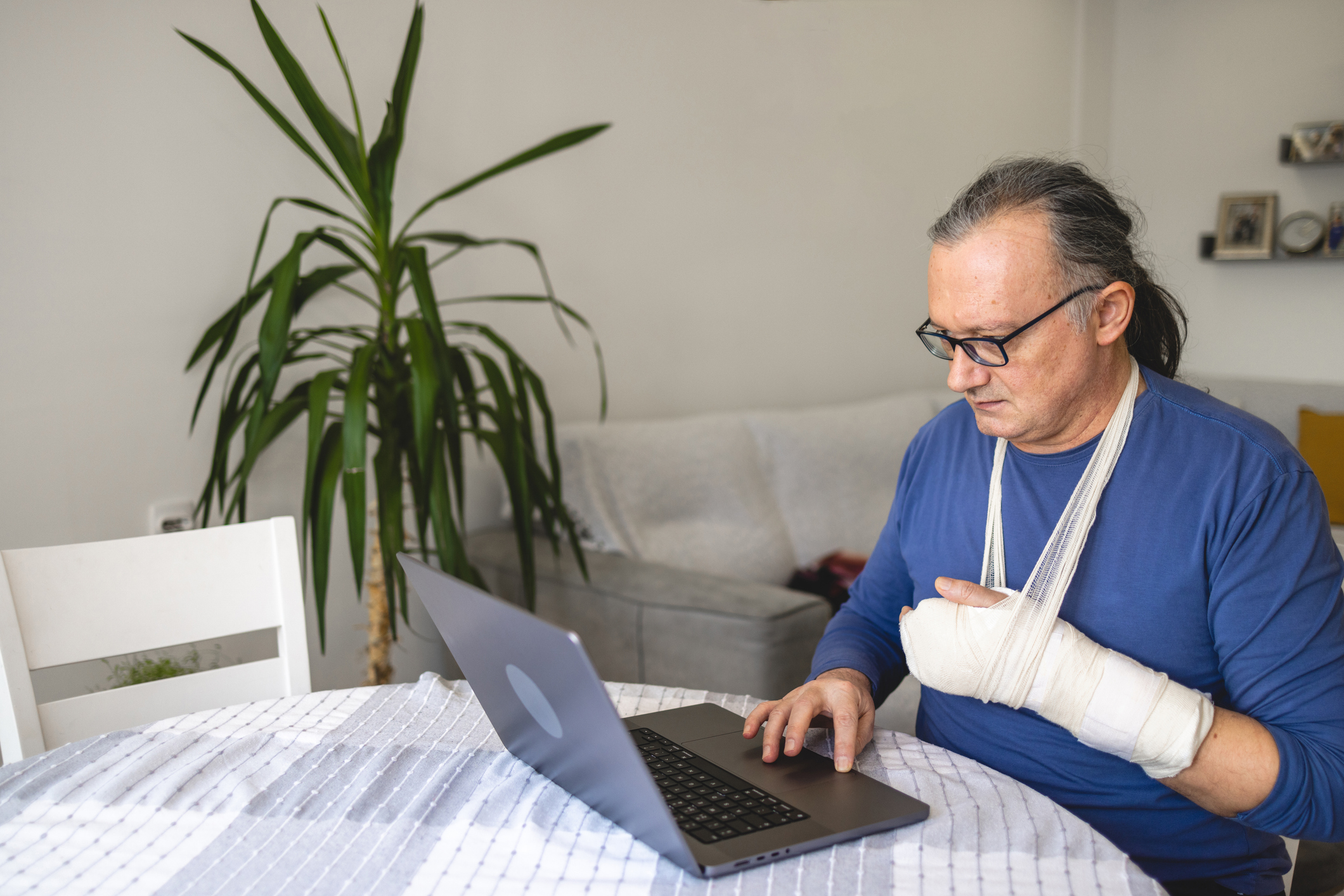 Senior or mid-adult Caucasian man, using a laptop while having a hand in the orthopedic cast