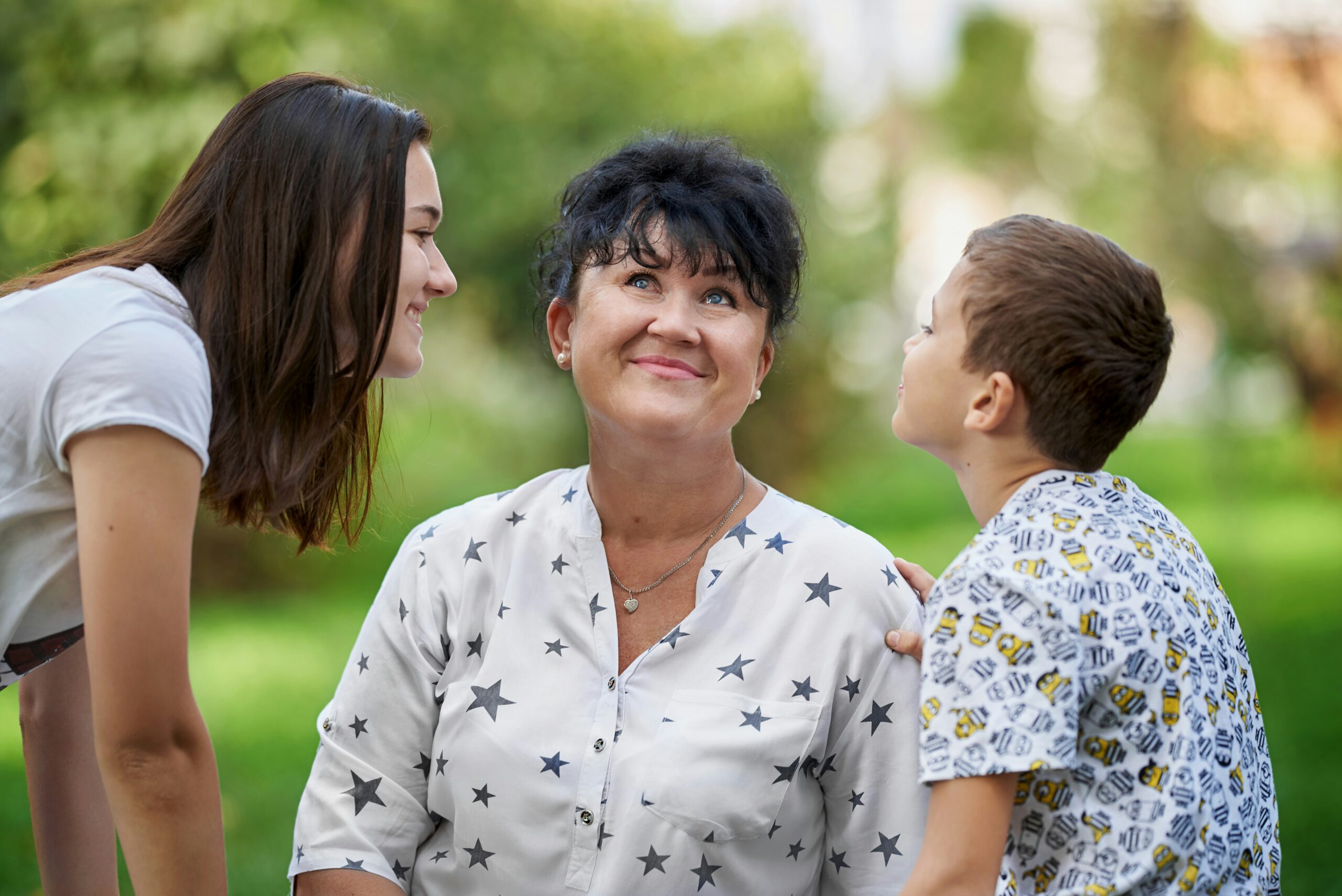 An older woman smiles while standing next to her daughter and grandson.