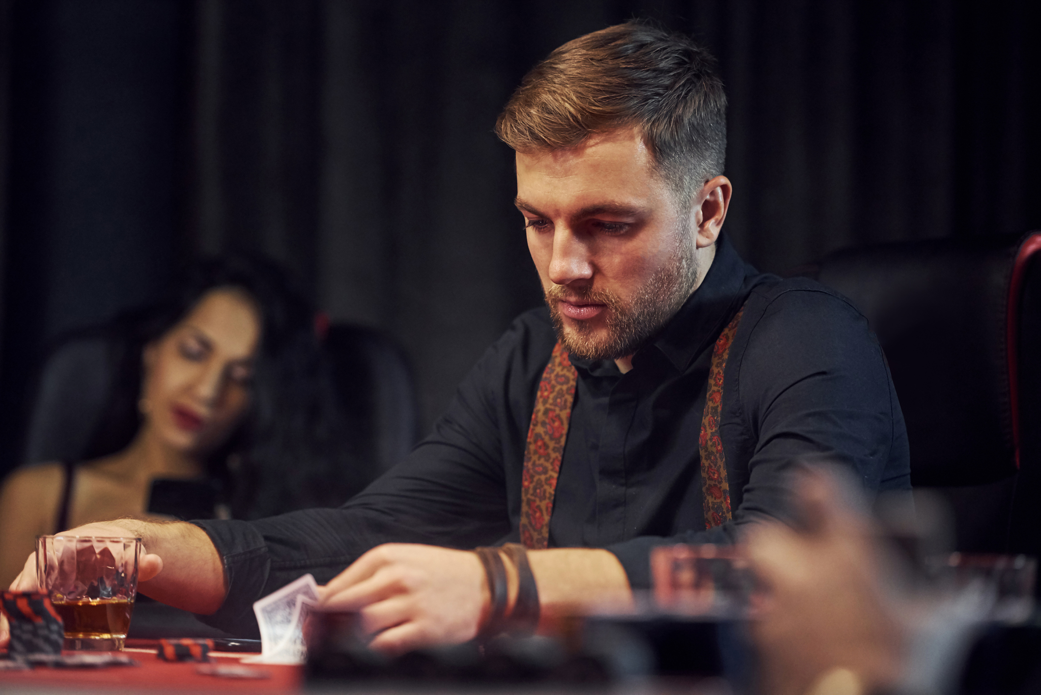 Elegant young people sitting by table, playing poker in casino