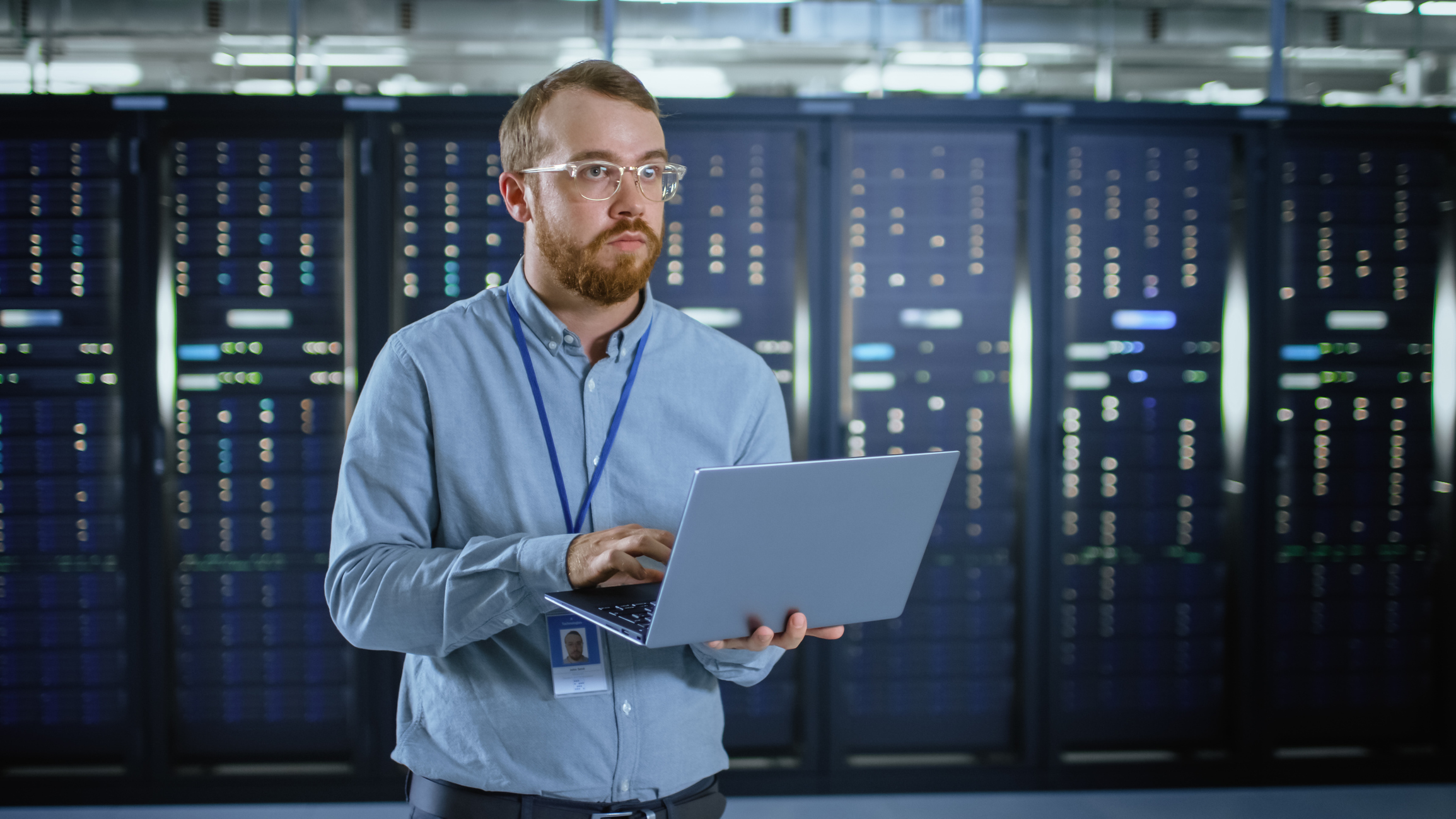 Engineer Working on Laptop in Data Center Next to Server Racks