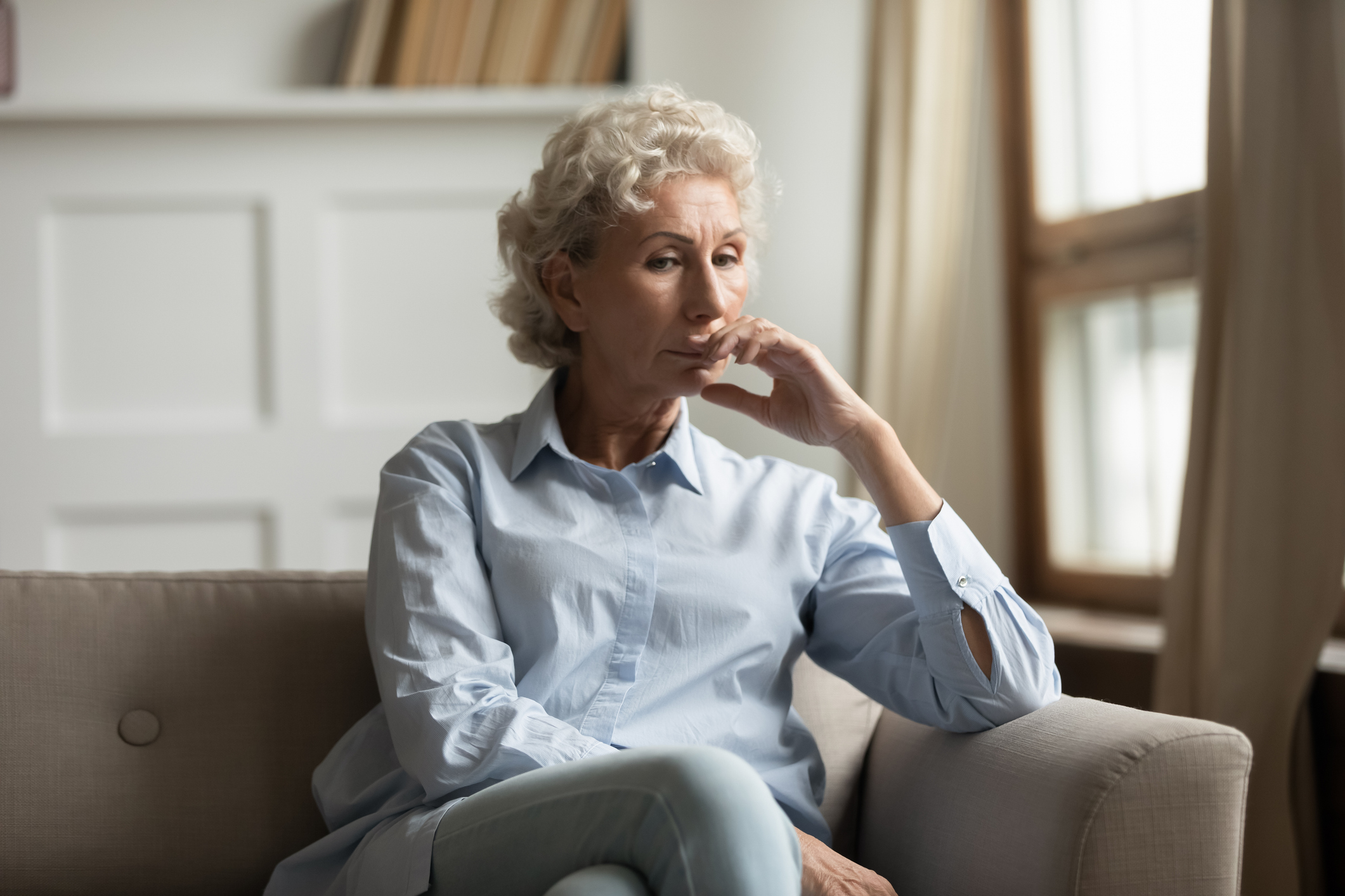 Sad unhappy middle aged female sitting on couch at home