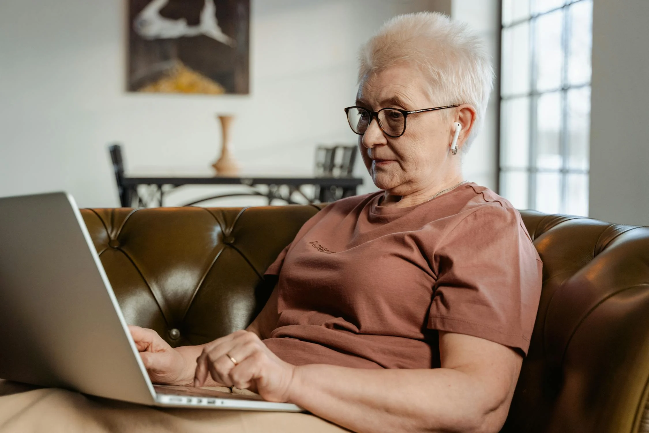 Senior woman sits on couch working on her laptop