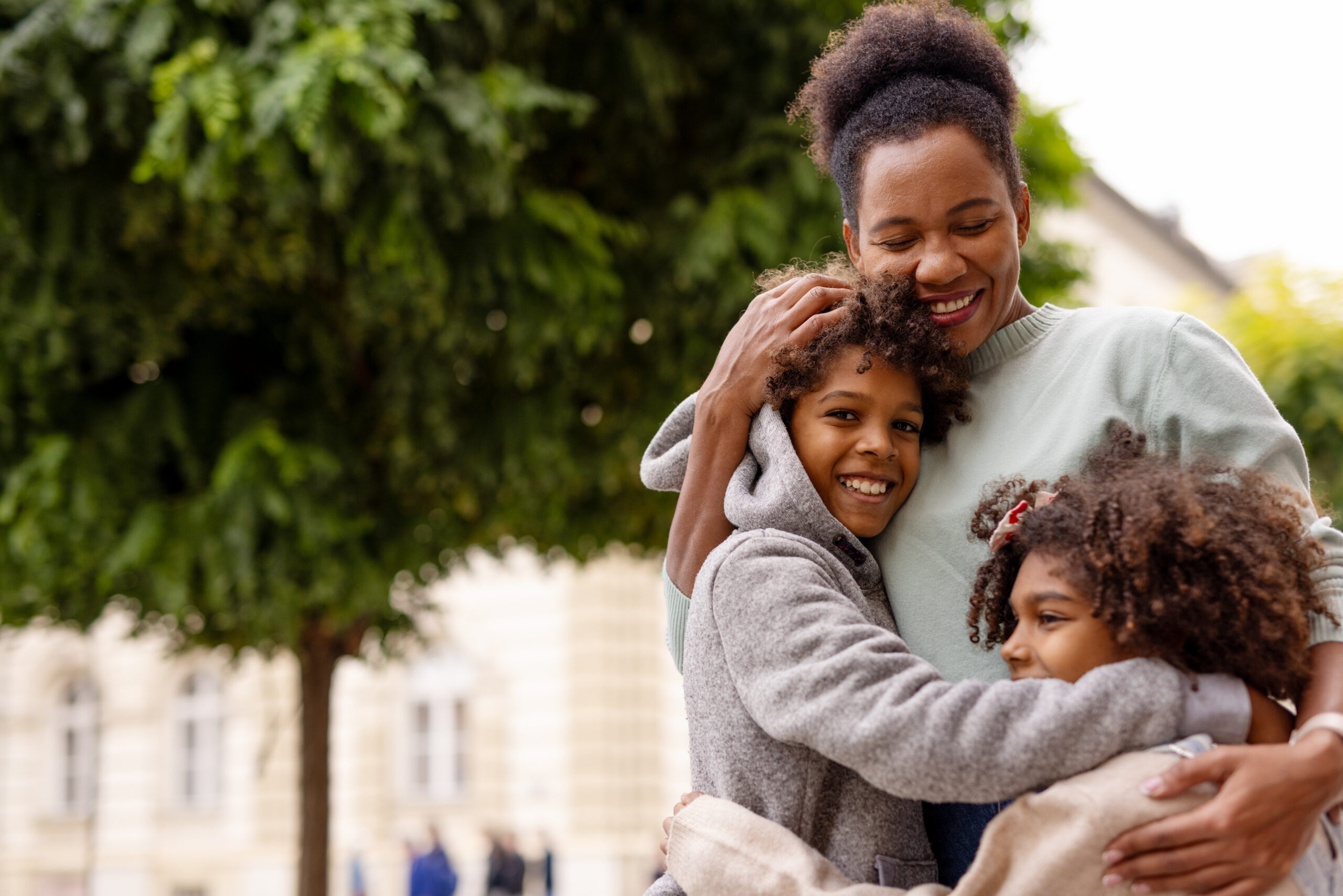 Happy African American family of single mom and two kids hugging each other.