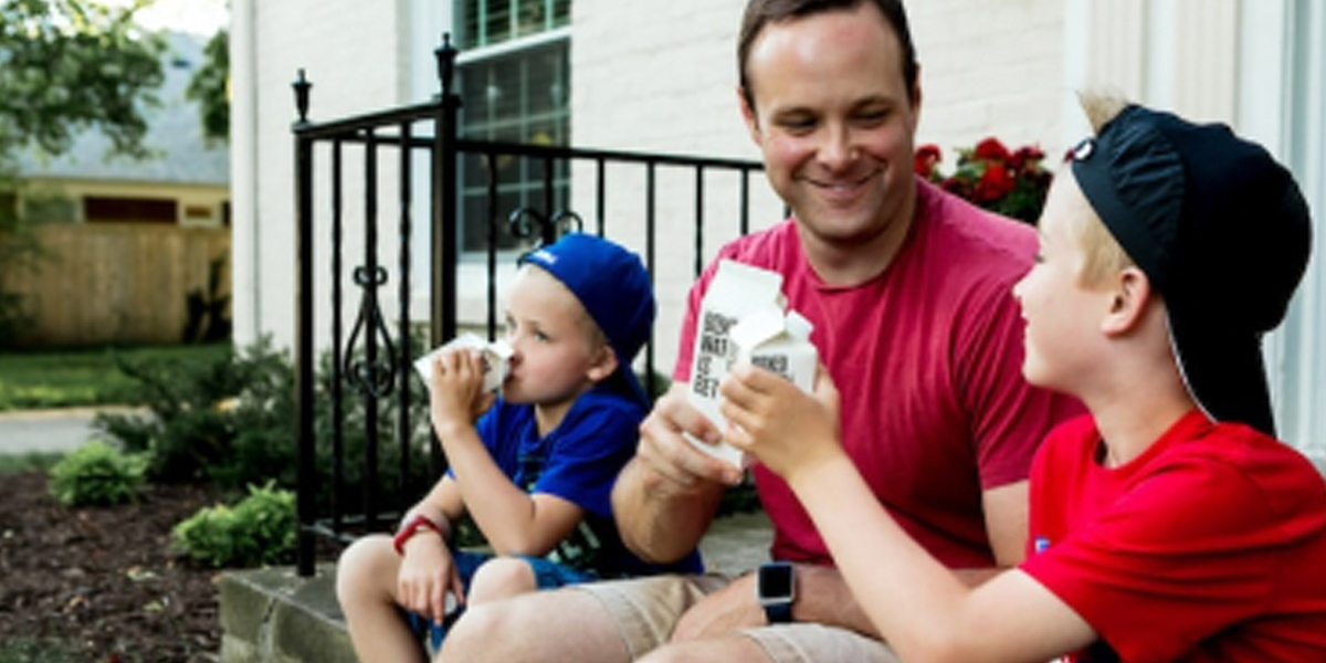 Dad sits on stairs with his two young sons enjoying beverages