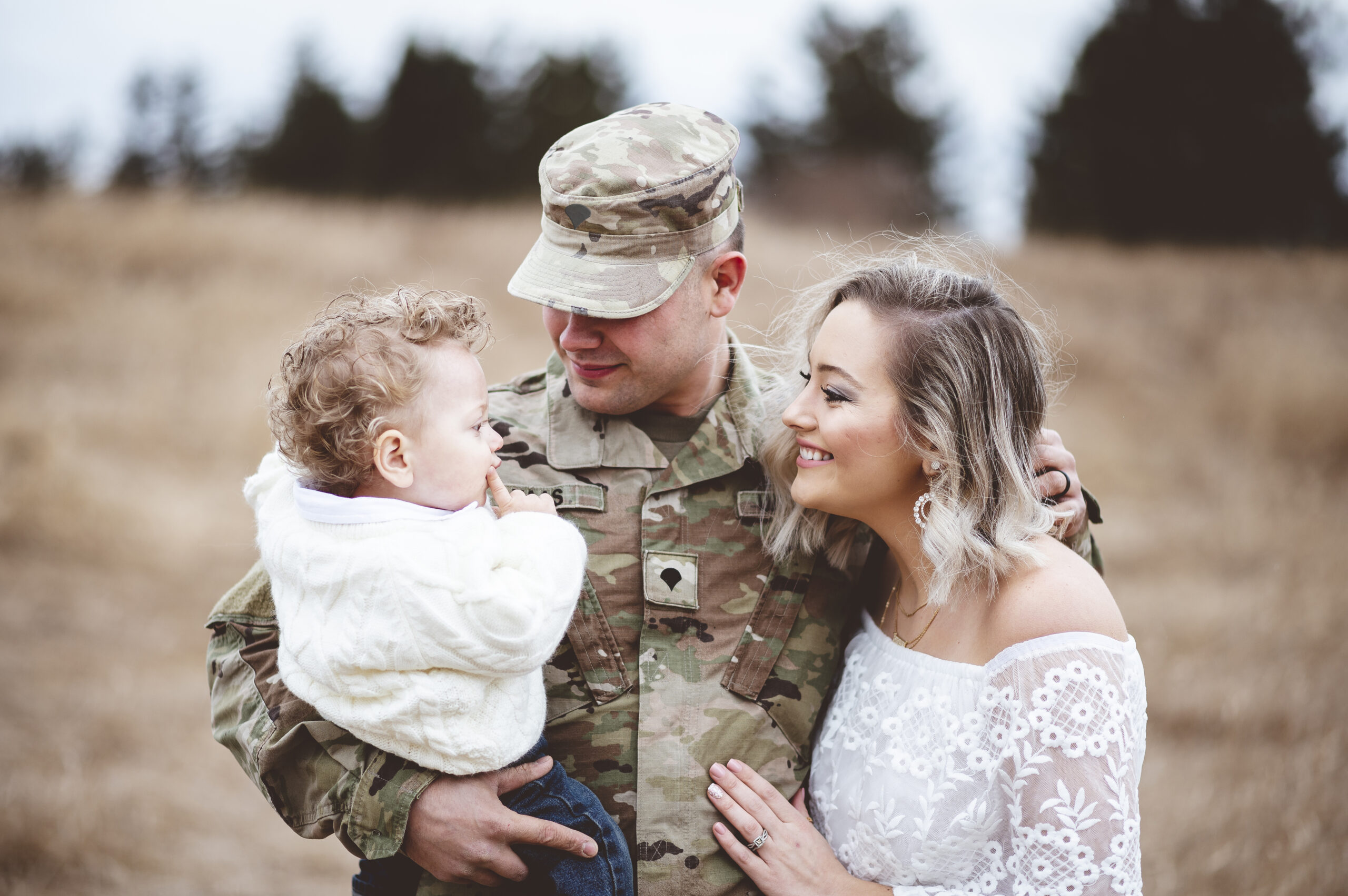 Military soldier happily poses with wife and baby boy in his arms.