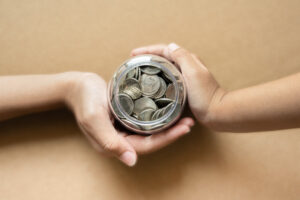 Kid hands holding coins in a jar together as saving concept for family or education.