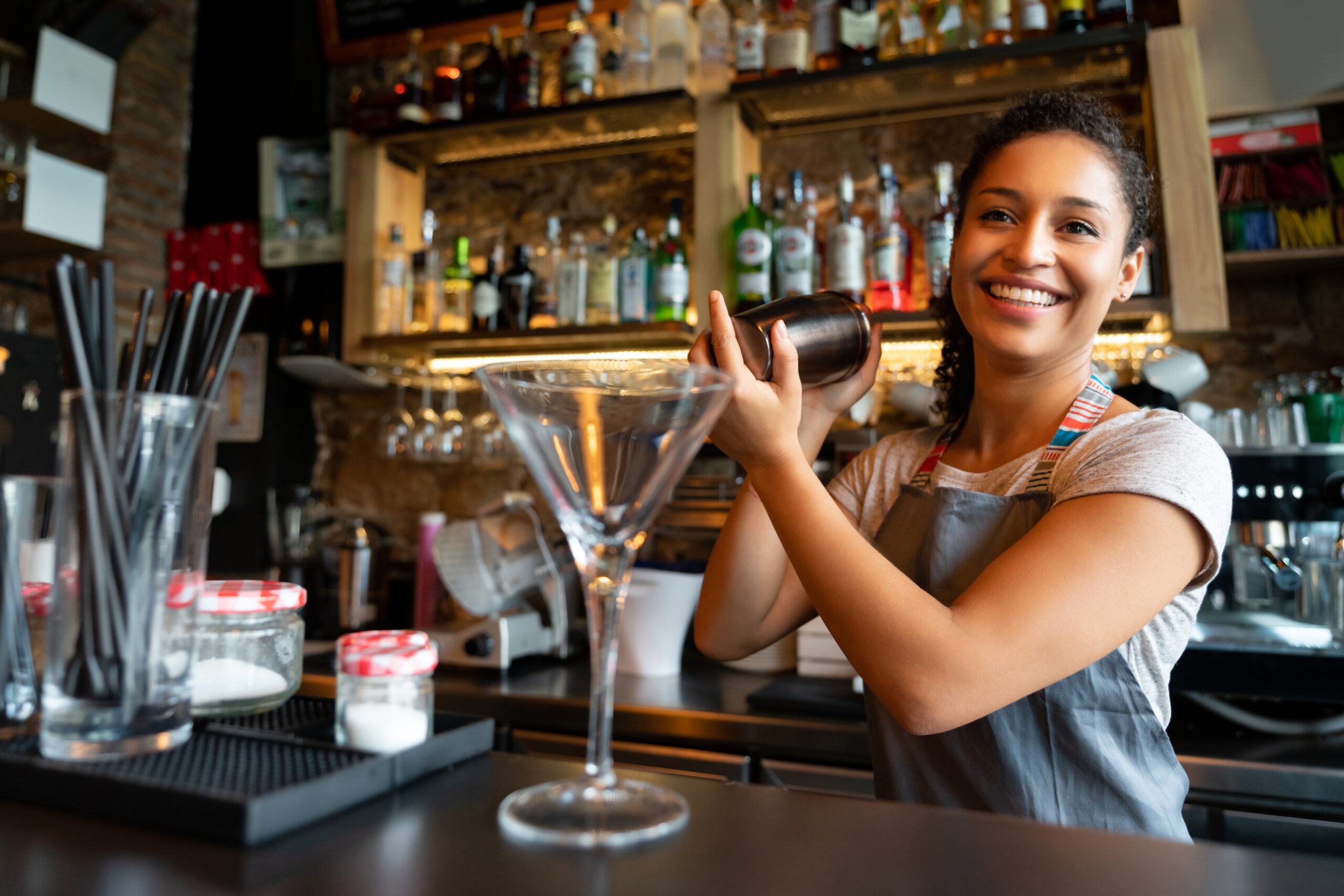 Bartender shaking mixing cup, preparing to pour a drink into a martini glass