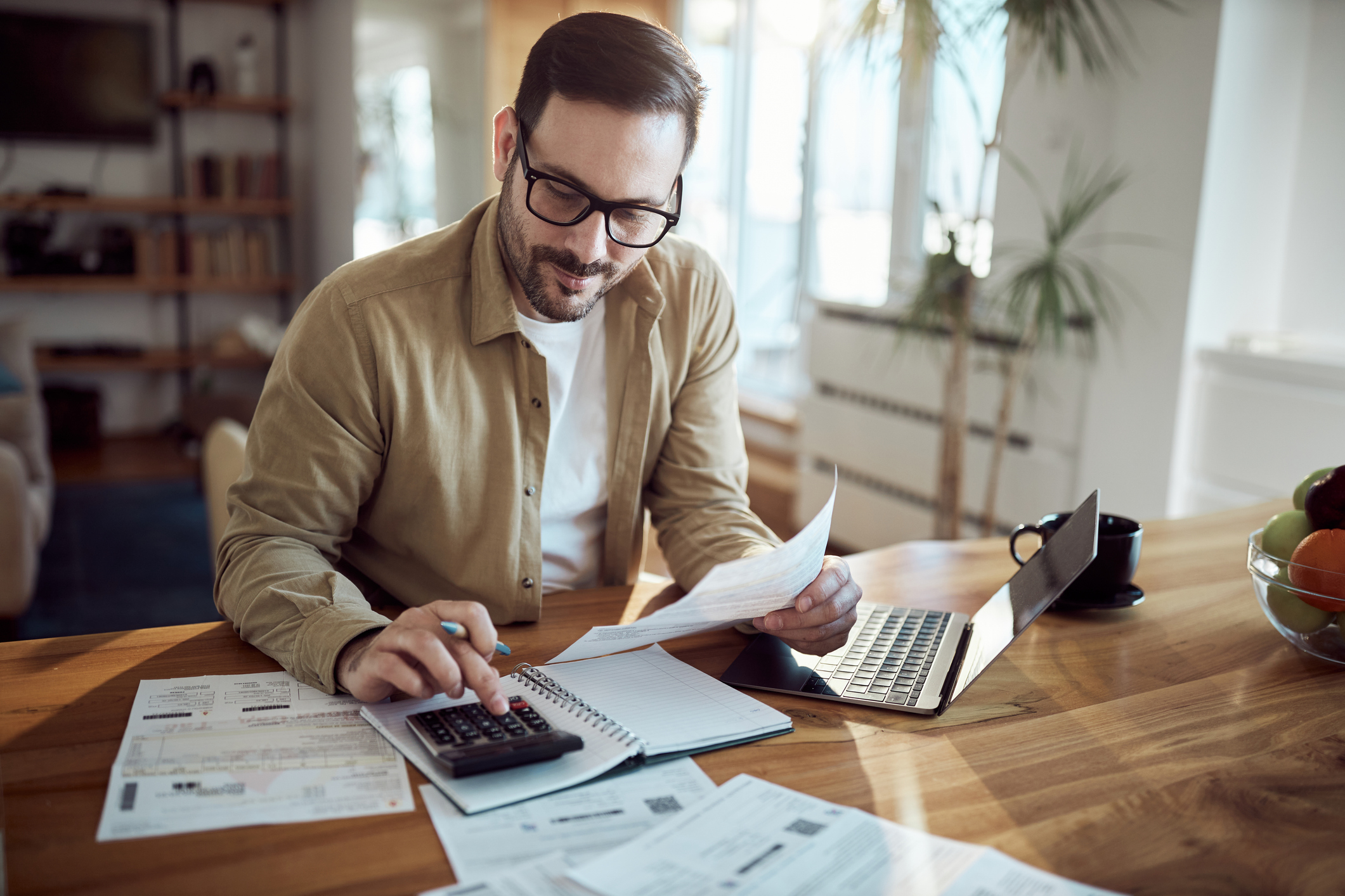 Young man using calculator while working on his financial plans and taxes at home.