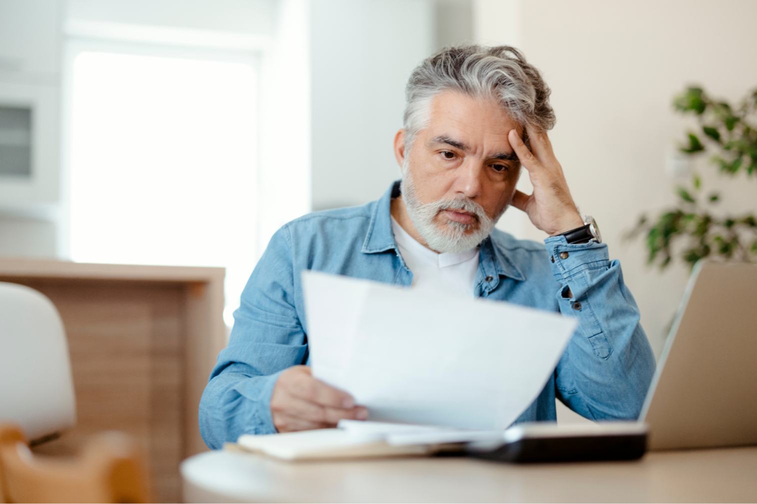 middle aged man doing paperwork A middle aged white man with gray hair appears frustrated with his income tax paperwork