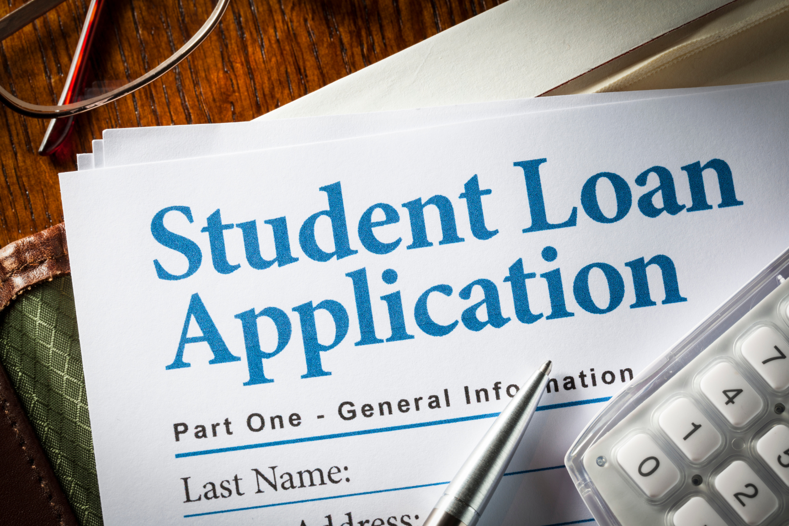 student loan application paperwork Student loan application paperwork, a pen, and calculator rest atop a desk.