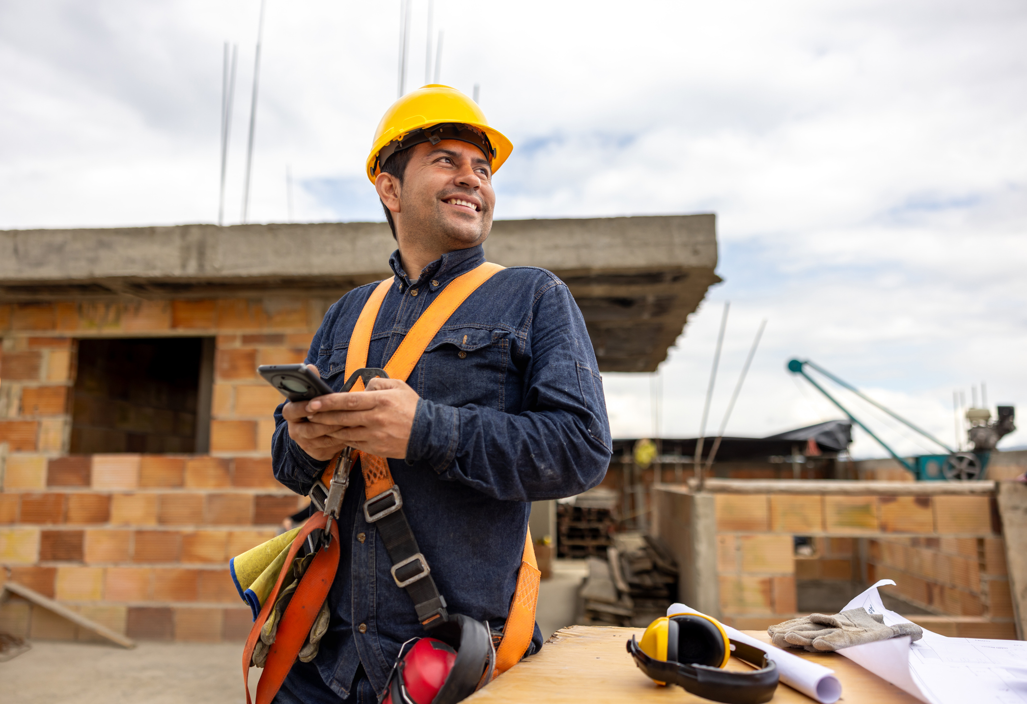 Construction worker smiling and using his cell phone at a building site