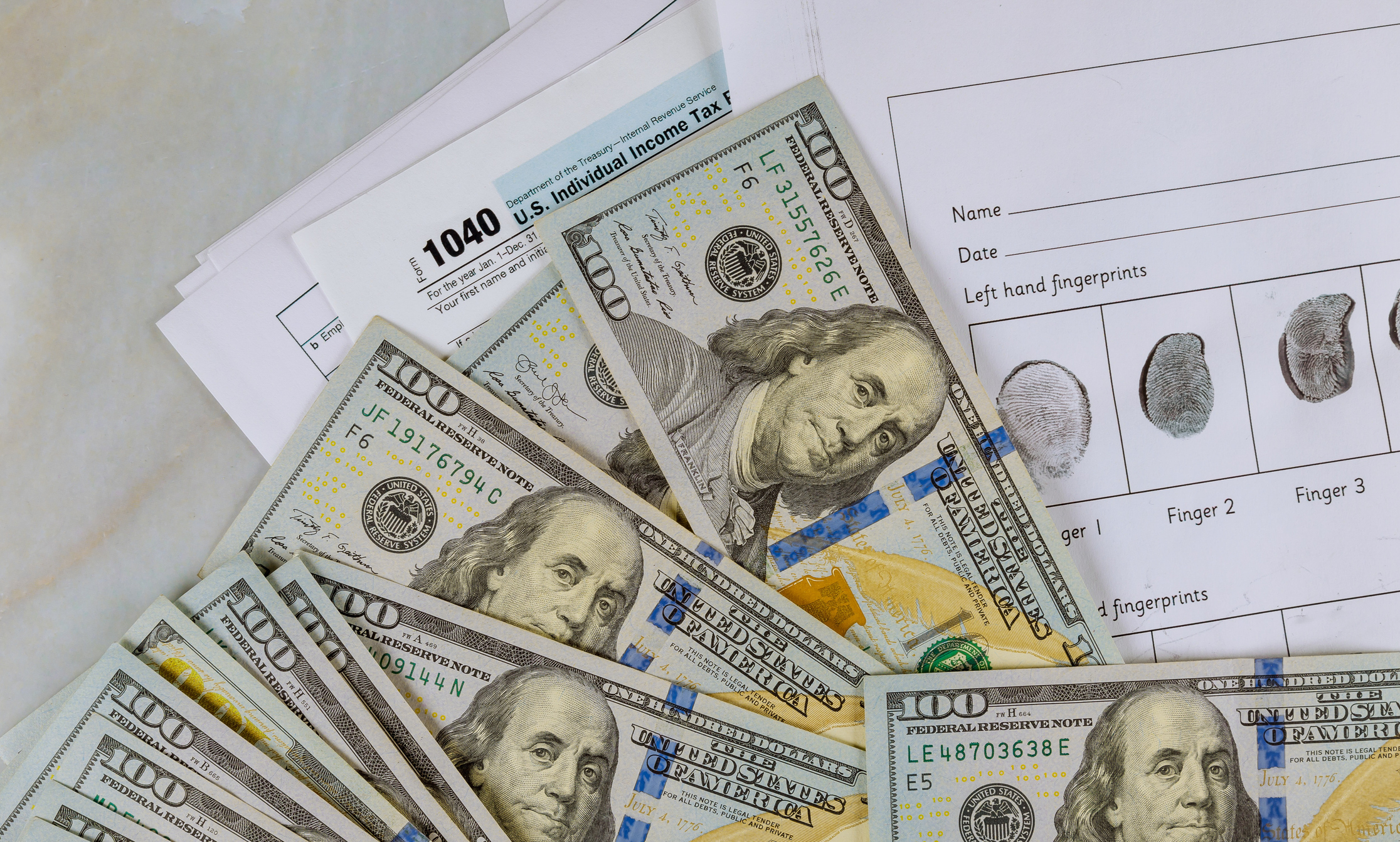 1040 individual tax return forms and 100 dollar bills on a desk.