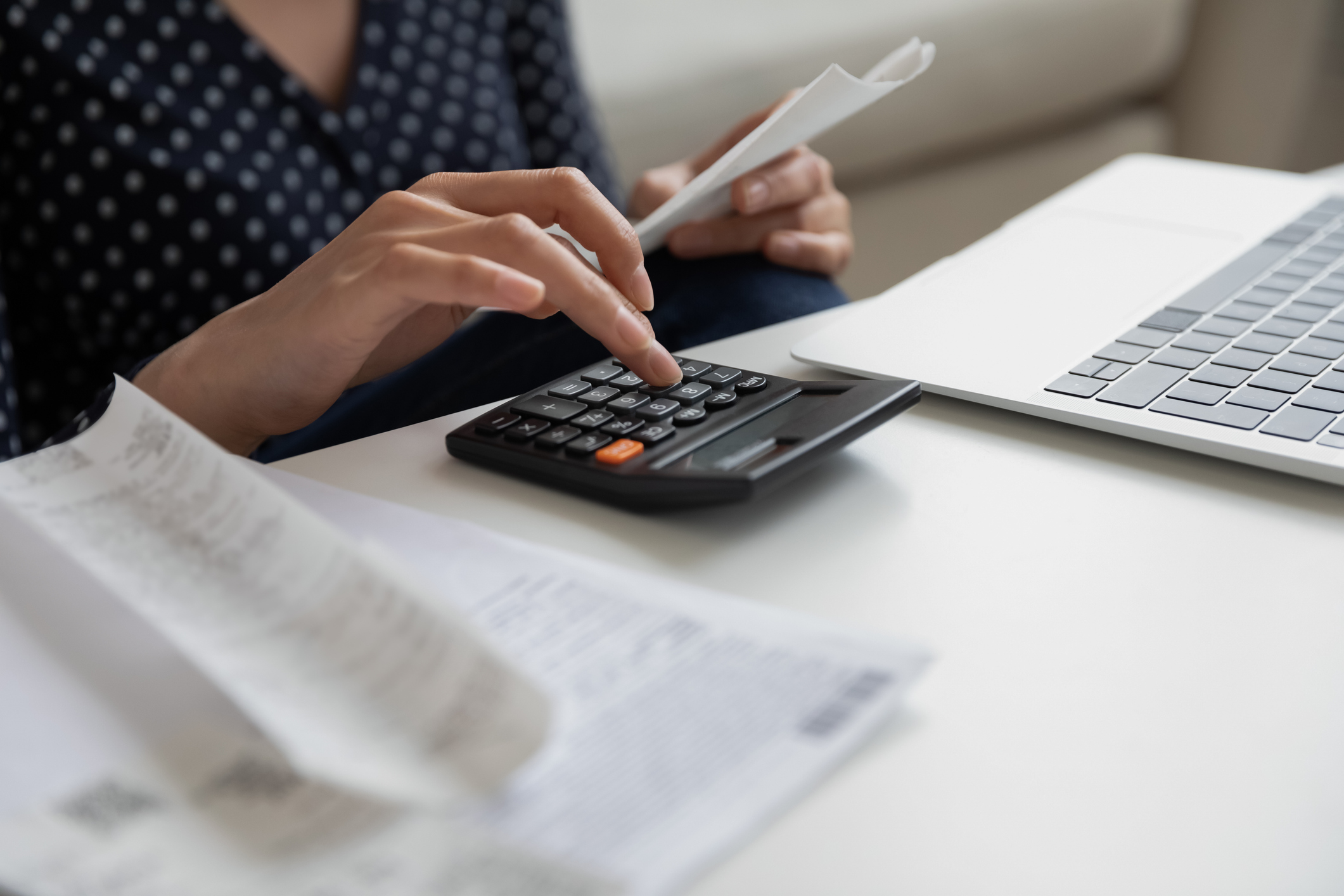 Close up woman calculating bills, using calculator, holding receipt