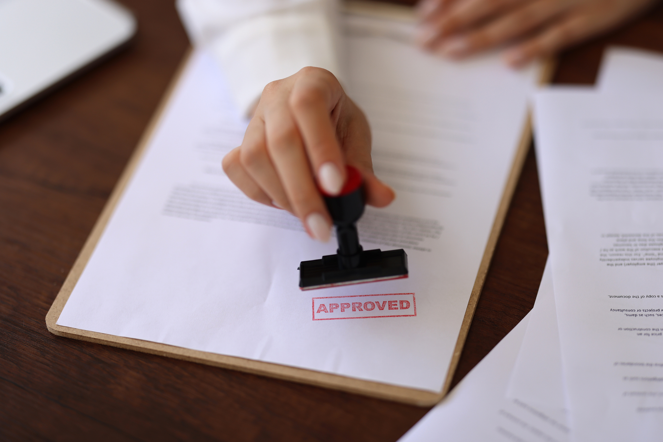 Close-cropped woman stamping "approved" on a tax accounting document while sitting at a desk.