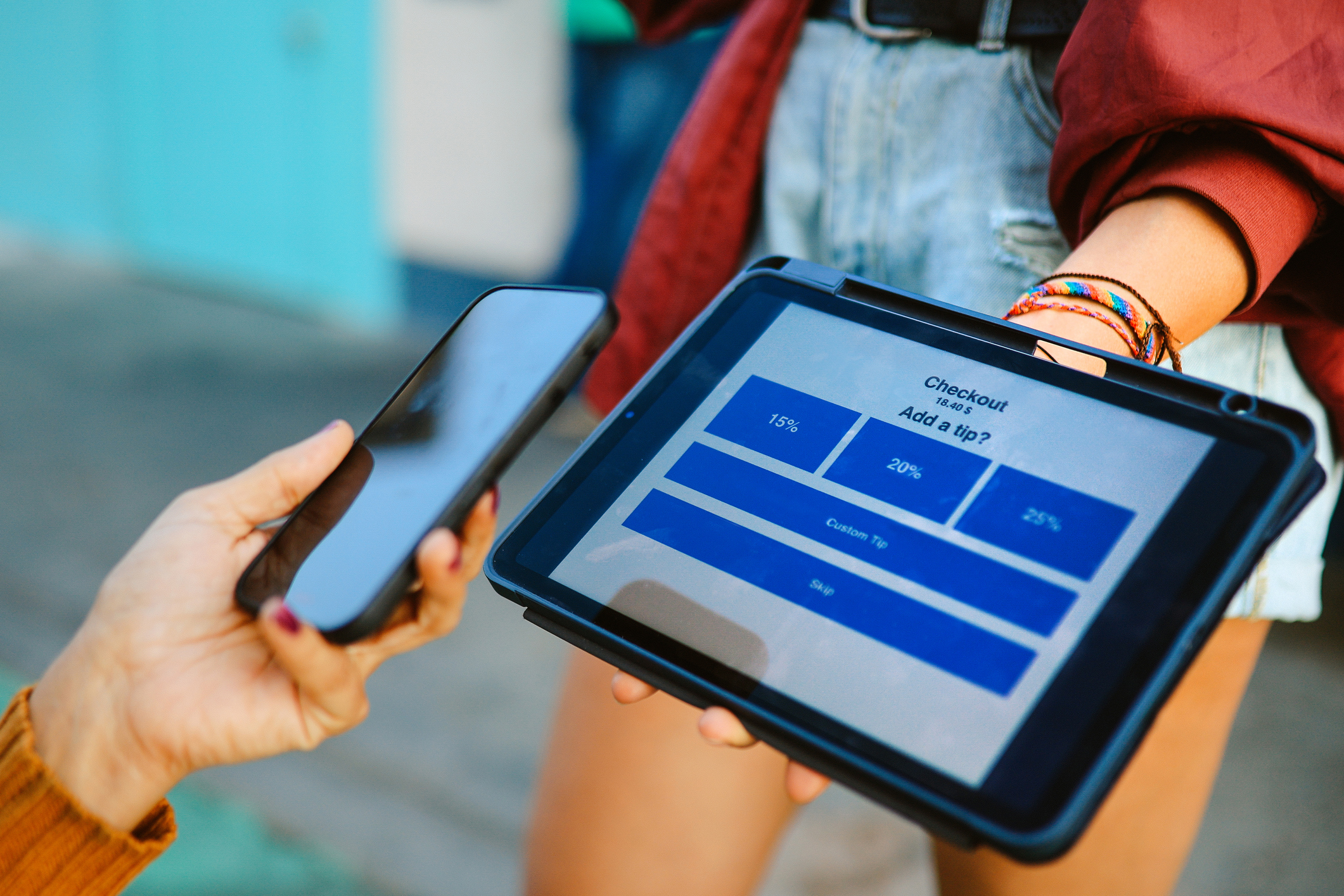 Woman uses digital tablet to pay and tip a barista. Smart phone tech and contactless payment concepts.