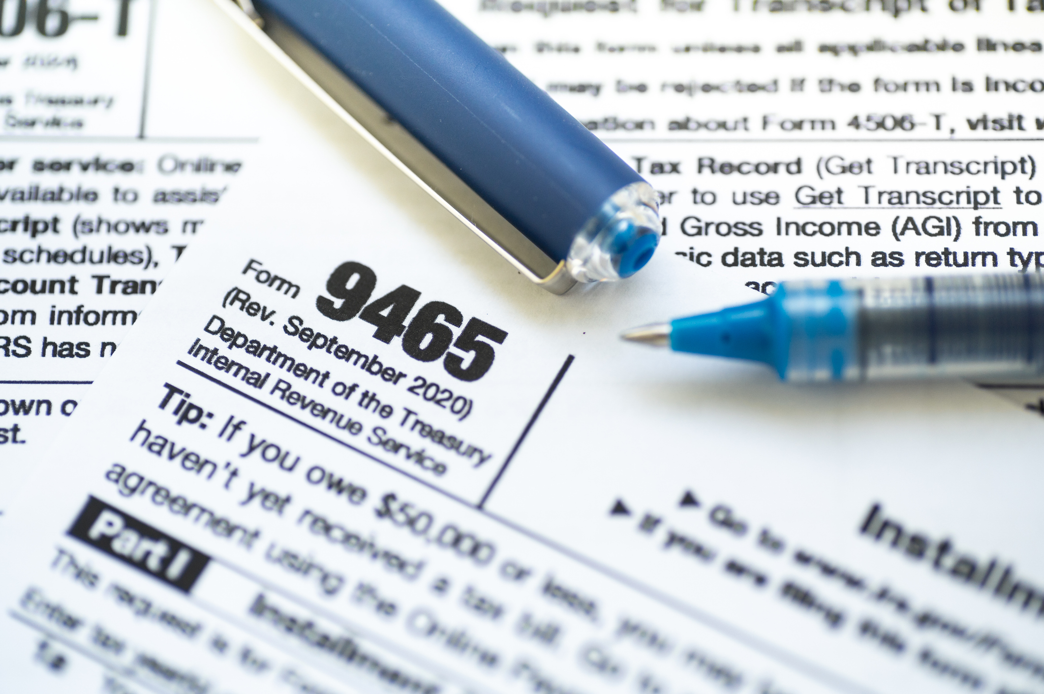 Two pens rest on a stack of IRS forms 9465.